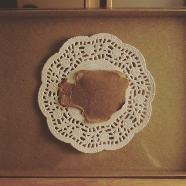51: Hand-torn brown paper teacup shape mounted on a white doily