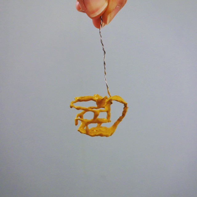 66: Tiny hanging three-dimensional sculpture of a teacup made with acrylic paint dripped over a wire frame