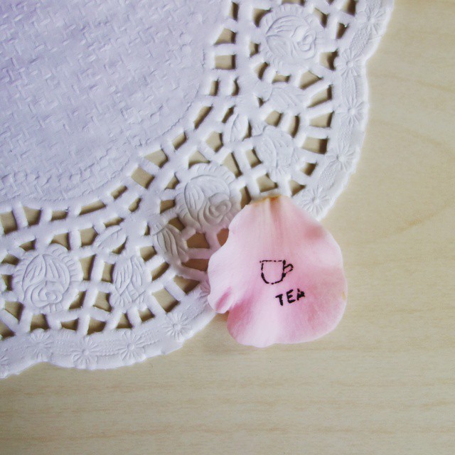 77: A simple teacup and the word tea drawn in black ink onto a pink Camellia petal