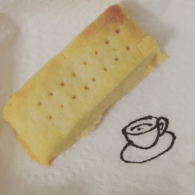 80: Black ink line drawing of a teacup on paper napkin next to a piece of shortbread biscuit
