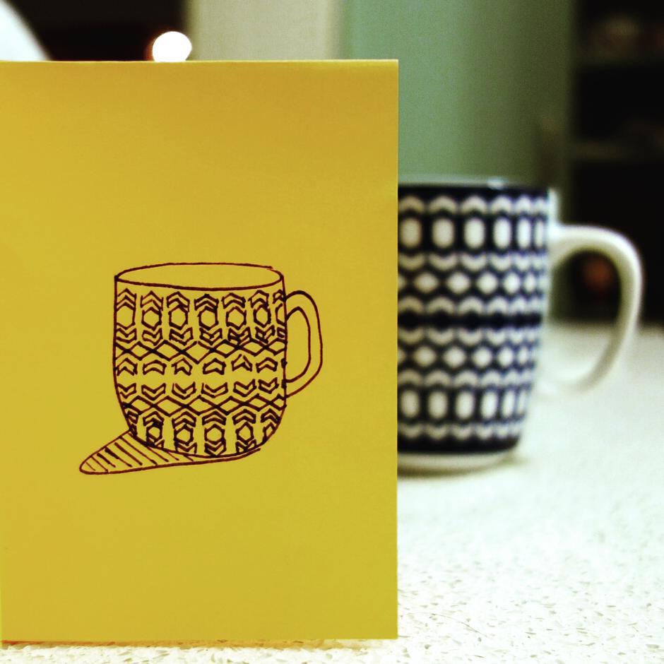 89: A black ink drawing of a patterned teacup on yellow paper, actual patterned teacup in background