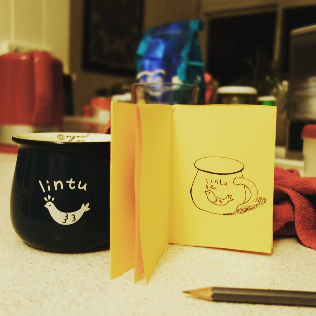 92: Black ink drawing of a teacup on yellow paper, actual teacup in background is blue with the word Lintu