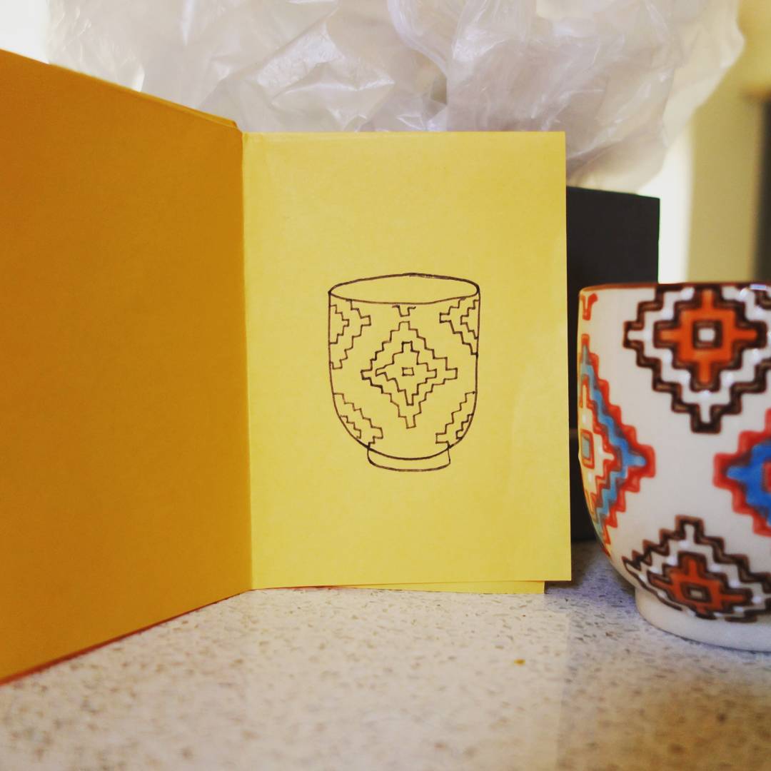 98: Black line drawing of a geometric patterned teacup on yellow paper, actual teacup next to the drawing