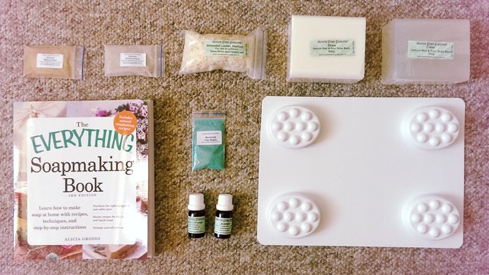 A soapmaking kit consisting of soap melts, exfoliants, essential oil, molds, and a how-to book